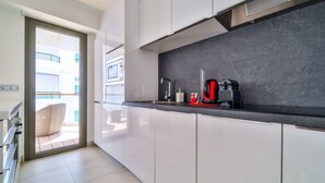 A modern kitchen with white cabinets, a black countertop, and a coffee machine. - 7 Croisette - Apartment 601 (Cannes)