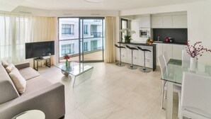 A modern living room with a sofa, a glass coffee table, a TV, and a balcony with a view of buildings. - 7 Croisette - Apartment 601 (Cannes)