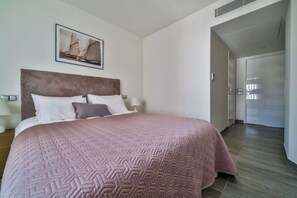 Een hotelkamer met een groot bed, een hoofdbord, een schilderij aan de muur en een deur naar een andere kamer.