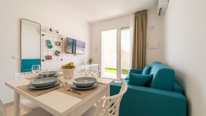 A modern living room with a teal sofa, a dining table with plates and cutlery, a large mirror, and a view of the outdoors. - GuestHost - Comfortable 40 sqm apartment, perfect for 4 people, located on the ground floor.The property is located inside the Borgo 81 Residence, a short distance from Marzamemi, and offers a quiet and well-served context, with a shared swimming pool, c (Pachino)