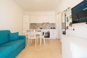 A compact kitchen with white cabinets, a dining table with chairs, and a teal sofa.