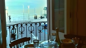 Un balcón con vistas a un lago y montañas, una mesa con una botella y una silla.