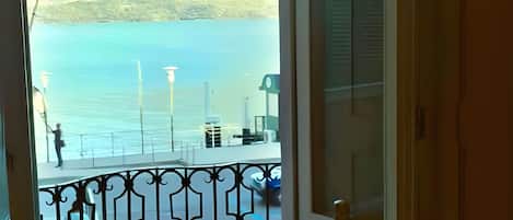 A balcony with a view of a lake and mountains, a table with a bottle, and a chair.
