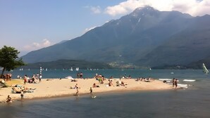 Una playa con gente, barcos y montañas al fondo.