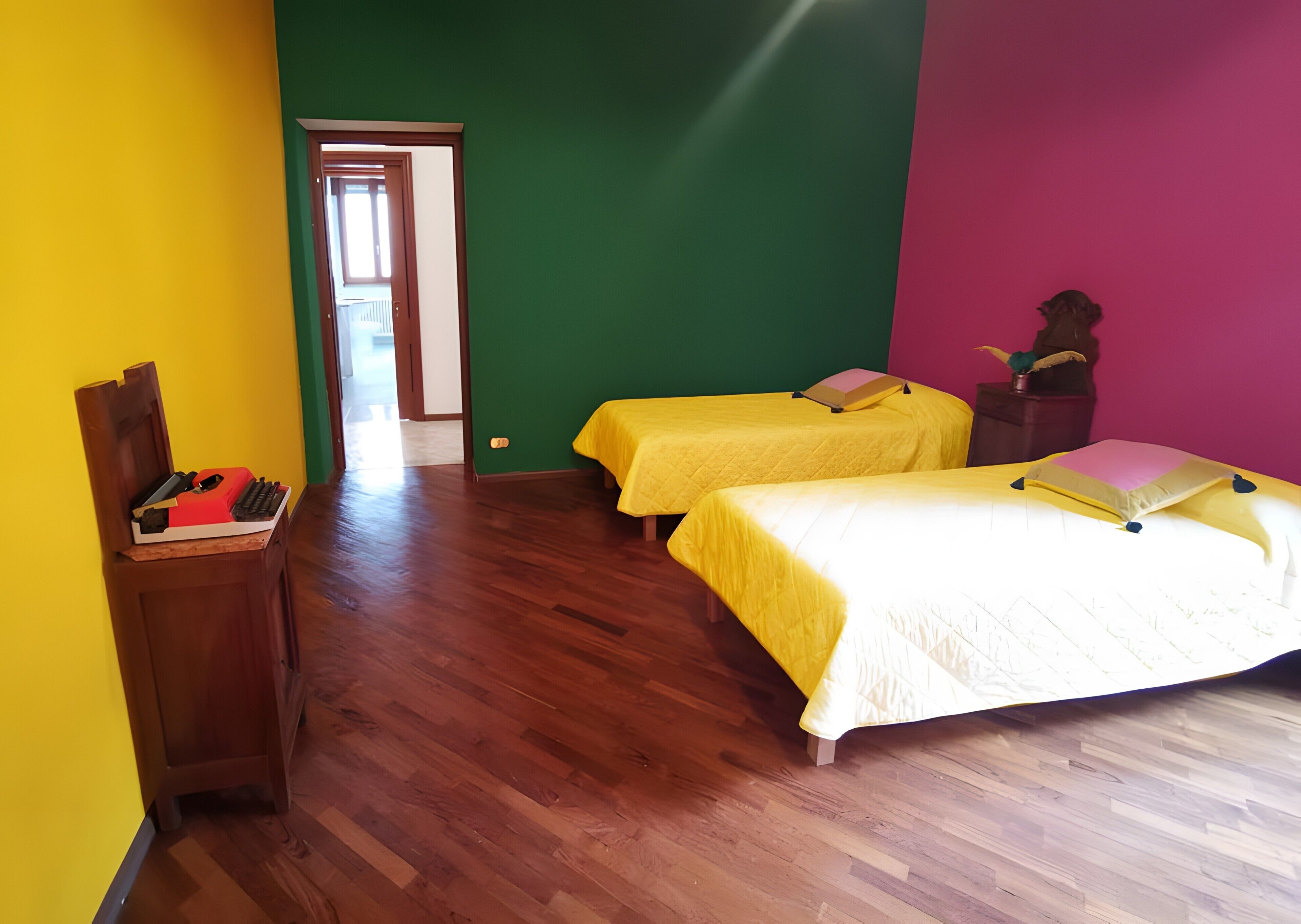 Una habitación con dos camas, un escritorio con silla y una puerta que da a otra habitación.