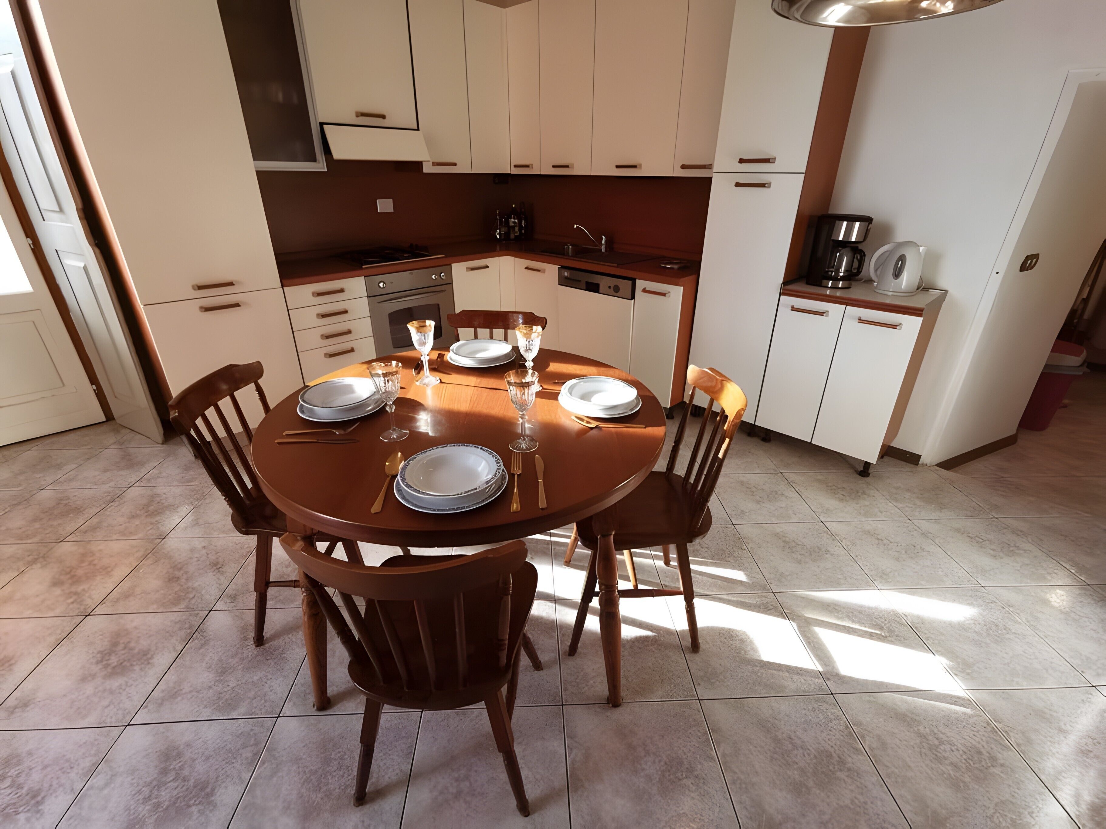 Un espace repas avec une table ronde dressée pour quatre personnes, entourée de chaises en bois.