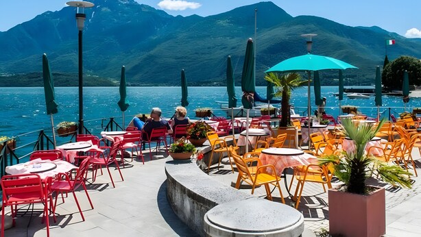Een terras met tafels en stoelen, een uitzicht op een meer, en bergen op de achtergrond.
