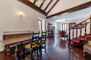 A spacious room with a wooden staircase, a dining table with chairs, and a large wooden cabinet.