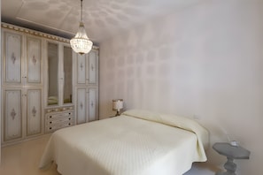 Une chambre à coucher avec un grand lit, une armoire ornée de panneaux décoratifs, un lustre et une table de chevet avec une lampe.