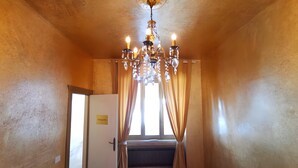 Un couloir avec un lustre, un radiateur et une porte sur laquelle est apposée une pancarte.