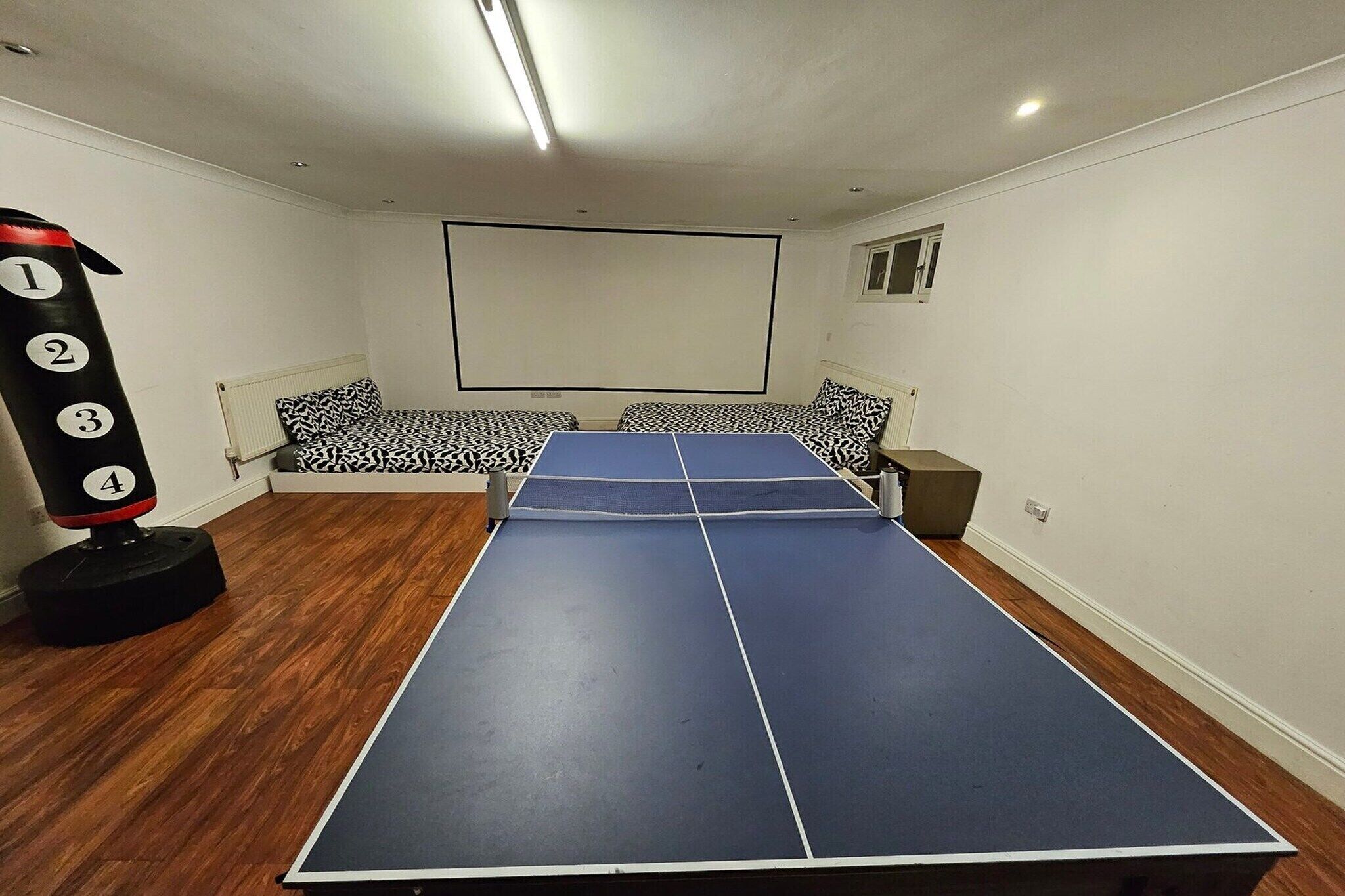 Um quarto com mesa de pingue-pongue, saco de pancadas e tela de projeção.