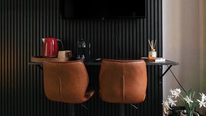 A modern room with a black wall, a flat-screen TV mounted above a black table, two brown leather chairs, and a potted orchid plant.