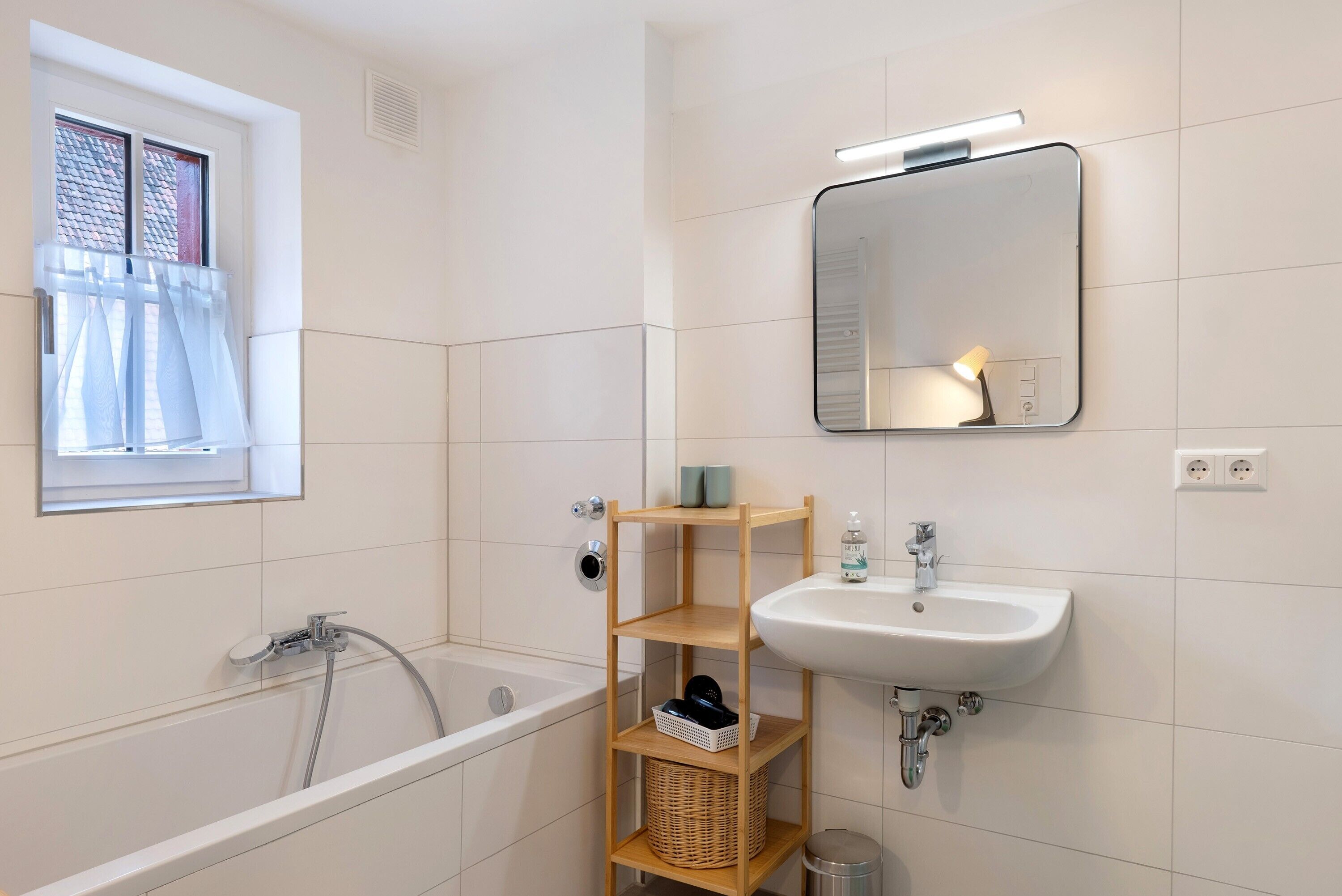 A modern bathroom with a bathtub, a sink, a mirror, and a window with a curtain.
