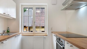 Una cocina moderna con armarios blancos, encimera de madera, horno empotrado y ventana con vistas a edificios.