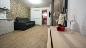 A modern living room with a wooden floor, a sofa, a dining table with a wine bottle and glasses, and a kitchen area with cabinets and a stone wall. - Love Nest Siena: Romantic Suite with SPA & Jacuzzi (Toscana)