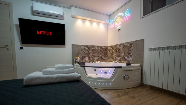 A modern hotel room with a flat-screen TV displaying 'NETFLIX', a jacuzzi, and a neon sign. - Love Nest Siena: Romantic Suite with SPA & Jacuzzi (Toscana)