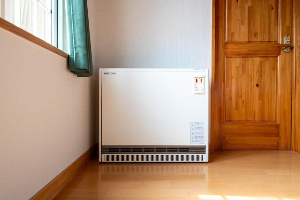 Een witte, draagbare airconditioner in een hoek van een kamer met houten vloeren en een houten deur.