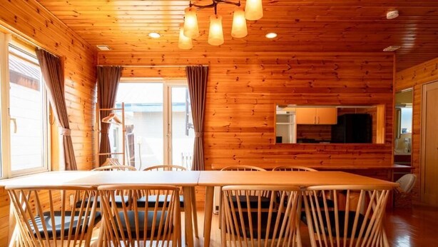 A wooden interior with a dining table and chairs, a kitchen area, and a view through a window.