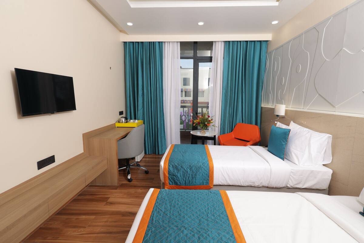 A hotel room with a bed, a desk, a chair, a TV, and a view of the outside.