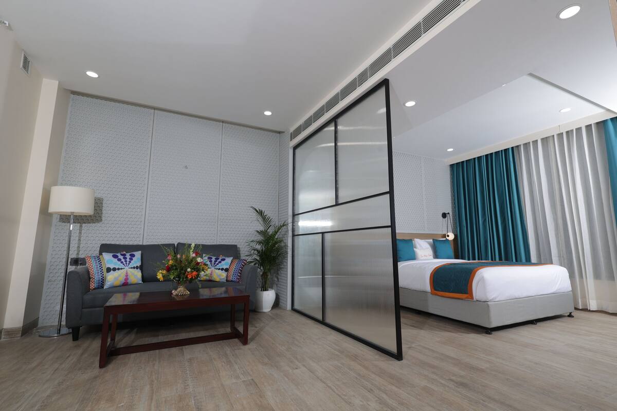 A hotel room with a sofa, a coffee table, a bed, and a large window with curtains.