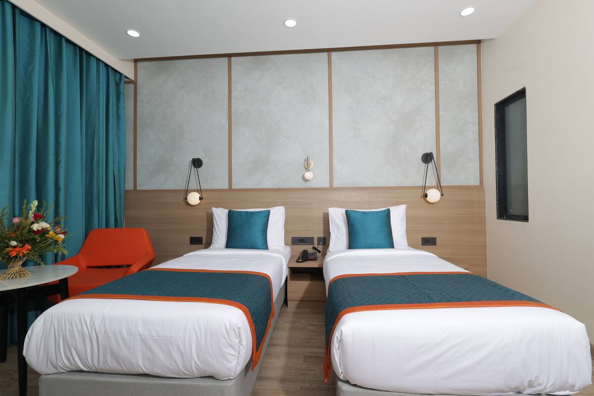 A hotel room with two beds, a small table with a vase of flowers, and a view of the city.