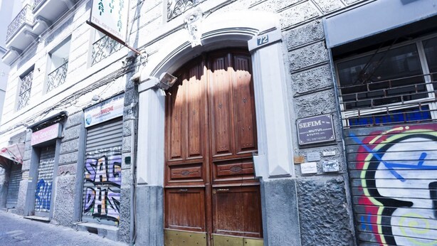A building with a large wooden door, a metal shutter, and a sign with a phone number. - GuestHost - La Casa del Presepe Central House (Naples)