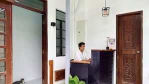 Una zona de recepción con un mostrador de madera, una planta en maceta y una puerta de madera con tallas intrincadas.