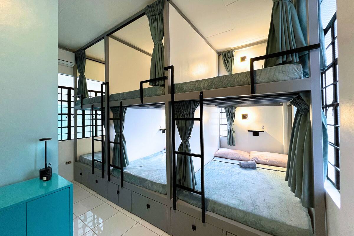 A bunk bed room with curtains, a small cabinet, and a window.