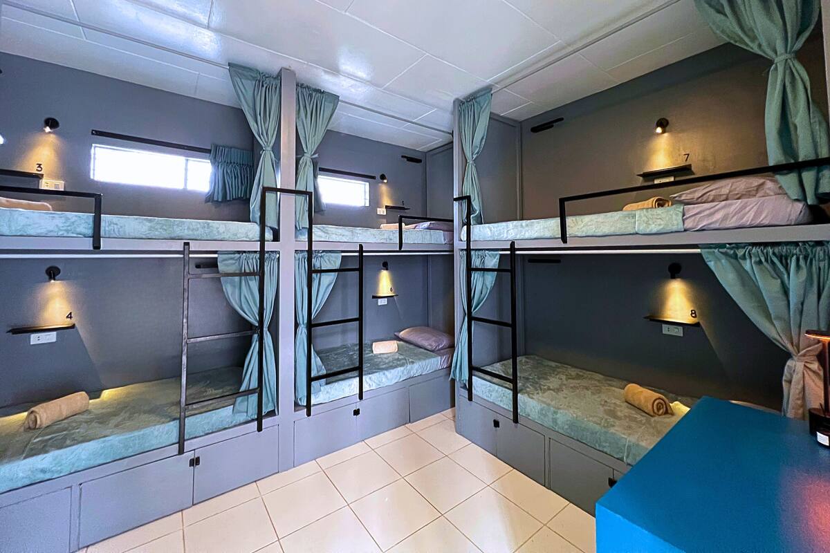 A dormitory room with bunk beds, curtains, and wall-mounted lights.