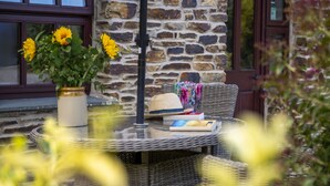 A wicker table with a vase of sunflowers, a hat, and a book. - Callestock Courtyard Cottages - Wheal Busy charming detached cottage perfect for your honeymoon (Truro)