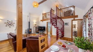 A cozy living room with a wooden staircase, a fireplace, and a dining area with a table set for two. - Callestock Courtyard Cottages - Wheal Busy charming detached cottage perfect for your honeymoon (Truro)