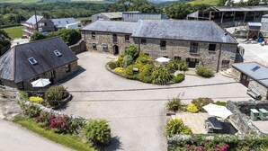 A stone building with a gravel courtyard, surrounded by greenery and a clear view of the countryside. - Callestock Courtyard Cottages - Wheal Busy charming detached cottage perfect for your honeymoon (Truro)
