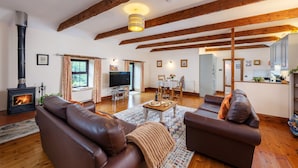 A spacious living room with a fireplace, leather sofas, a coffee table, and wooden beams on the ceiling.