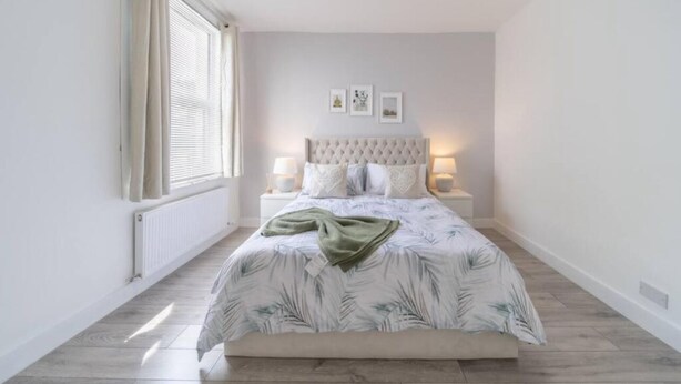 Un dormitorio con una cama grande, una ventana con cortinas, un radiador y tres cuadros en la pared.