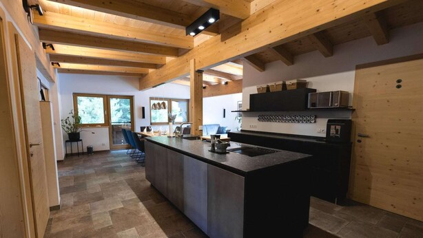 Una cocina moderna con una isla grande, vigas de madera y vistas al exterior.