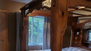 A wooden four-poster bed with a plaid bedspread, a wooden wardrobe, and a window with a view of trees. - Hot Tub and King bed with 3 other beds (Anchorage)