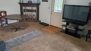 A living room with a TV, a fireplace, a door with a stained glass window, and a carpeted floor. - Hot Tub and King bed with 3 other beds (Anchorage)