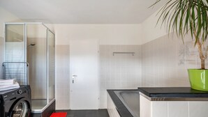 Ein modernes Badezimmer mit Dusche, Waschmaschine, Badewanne und einer Zimmerpflanze.