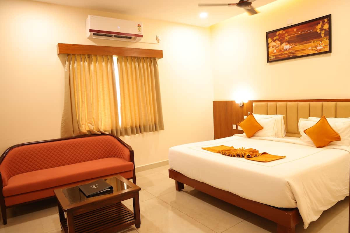Quarto de hotel com cama, sofá, mesa de centro, ar condicionado e um quadro na parede.