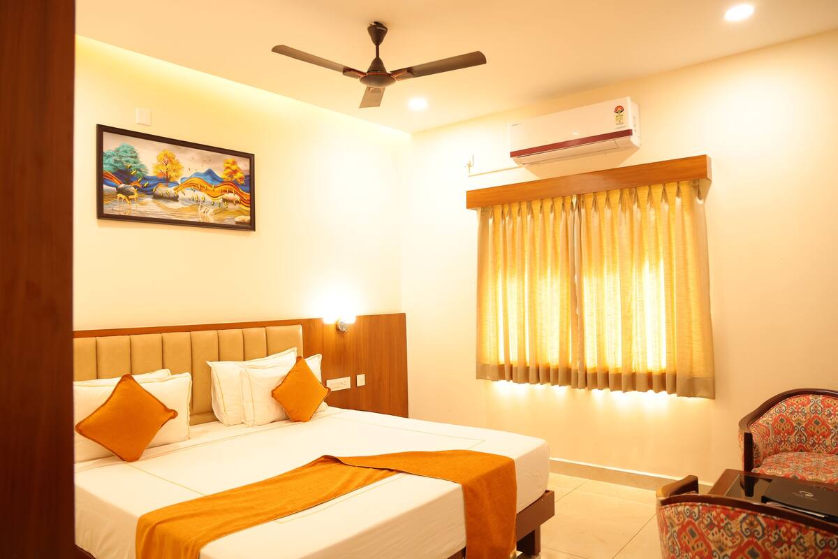 Quarto de hotel com cama, ventoinha no teto, ar condicionado, janela com cortinas e um quadro na parede.