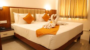 A hotel room with a bed, pillows, a blanket, and a heart-shaped towel arrangement.