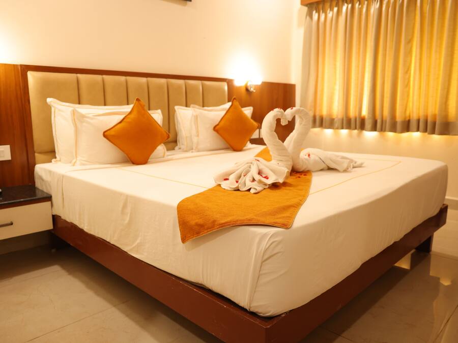 A hotel room with a bed, pillows, a blanket, and a heart-shaped towel arrangement.