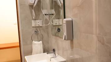 Un baño con lavabo blanco, toallero, secador de pelo y secamanos.