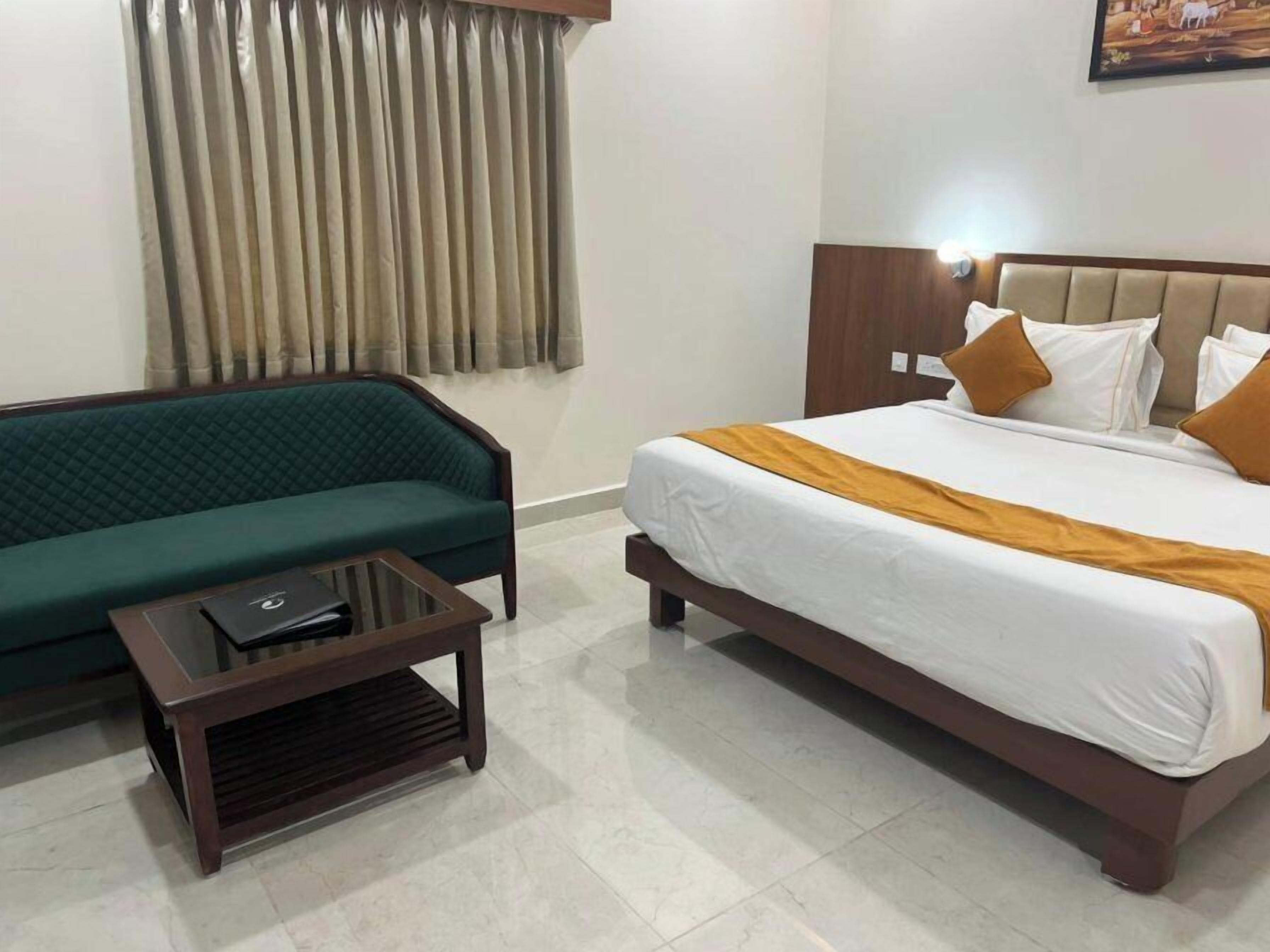 Ein Hotelzimmer mit einem Bett, einem grünen Sofa, einem kleinen Tisch und einem Fenster mit Vorhängen.