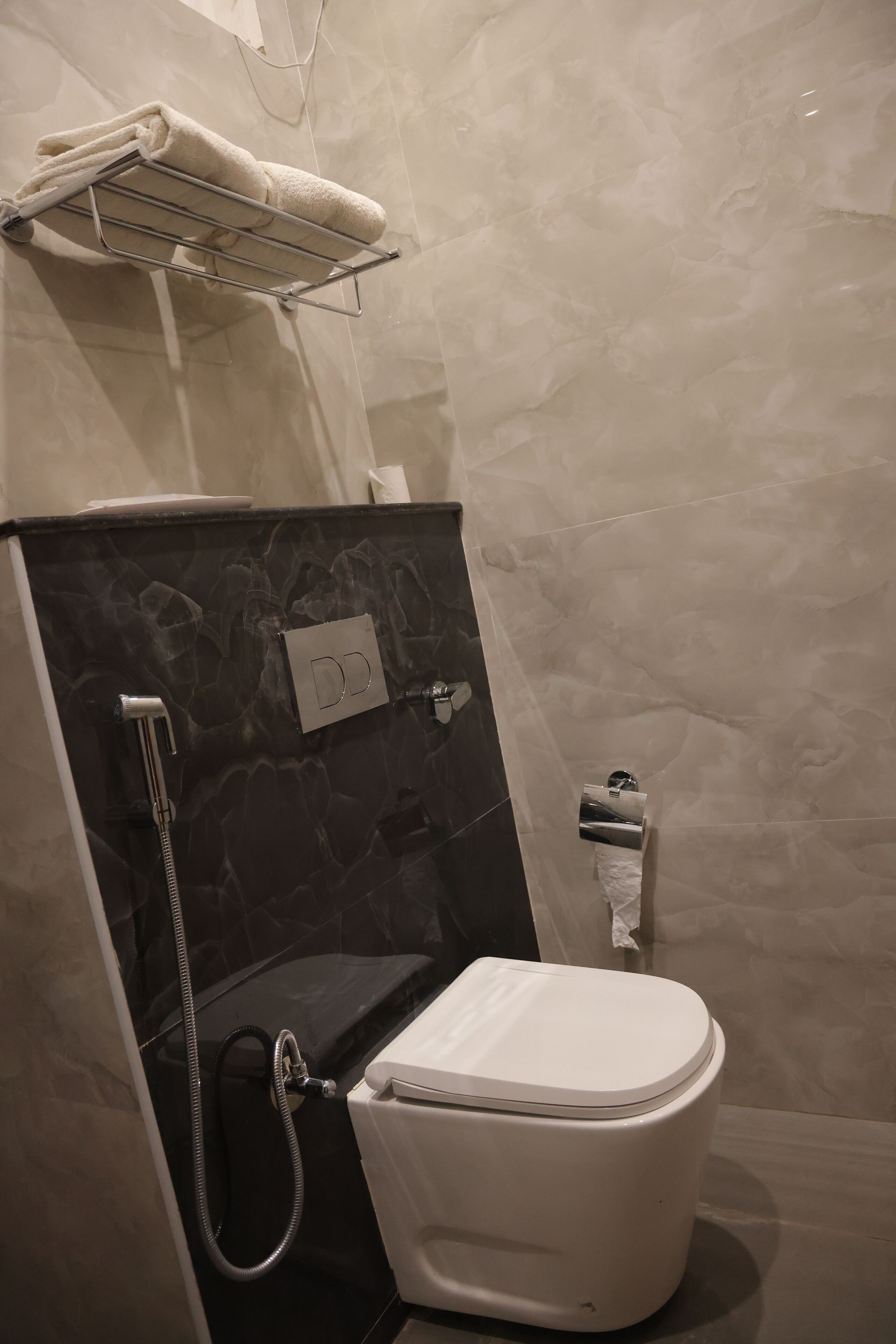 A bathroom with a toilet, a shower, a towel rack, and a toilet paper holder.