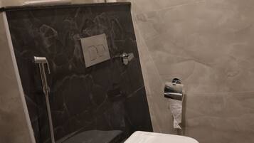 A bathroom with a toilet, a shower, a towel rack, and a toilet paper holder.