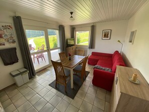 Ett rum med ett matbord, stolar, en röd soffa, en tv och ett fönster med gardiner.