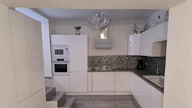 A modern kitchen with white cabinetry, a built-in oven, a microwave, a sink, and a decorative fan.
