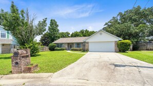 A single-story house with a garage, a front yard with a lawn and a brick mailbox, and a wooden fence in the background. - Tranquil Haven | Pet Friendly (Pensacola)