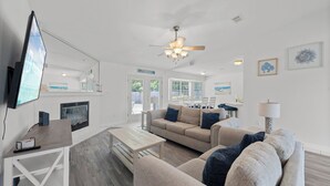 A modern living room with a sofa, coffee table, and TV. There is a fireplace, ceiling fan, and artwork on the walls. - Tranquil Haven | Pet Friendly (Pensacola)